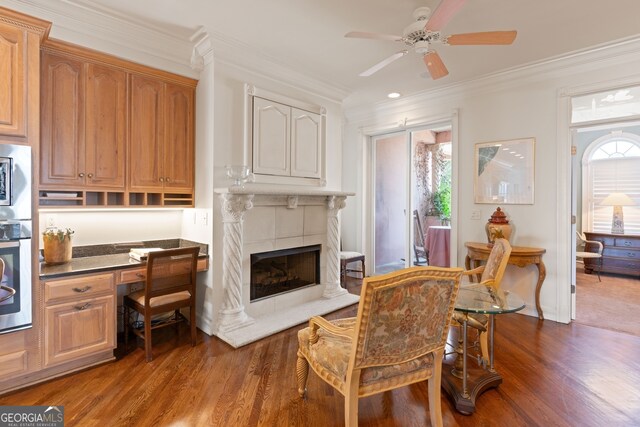 interior space with ceiling fan, a tiled fireplace, dark wood-type flooring, and crown molding