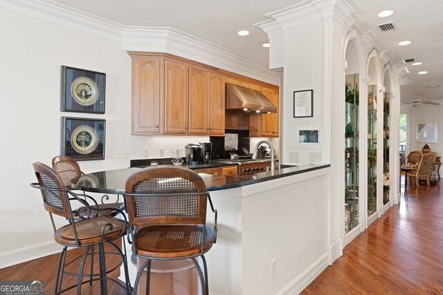 kitchen featuring exhaust hood, dark wood-type flooring, a kitchen breakfast bar, kitchen peninsula, and crown molding
