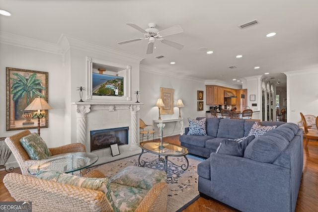living room with ceiling fan, hardwood / wood-style floors, a tile fireplace, and crown molding