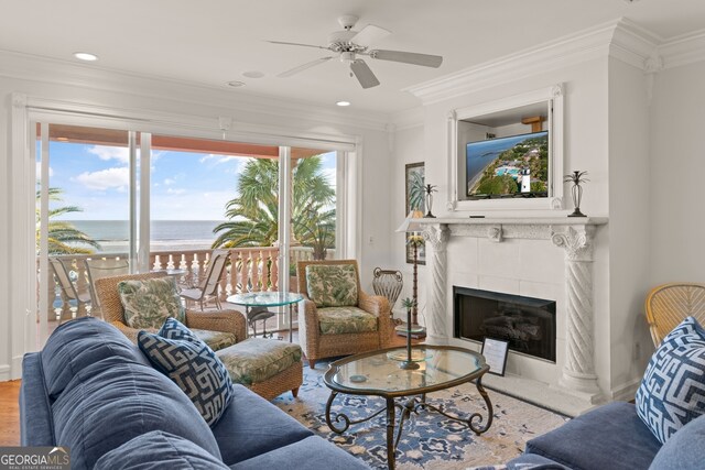 living room featuring ceiling fan, ornamental molding, and a tiled fireplace