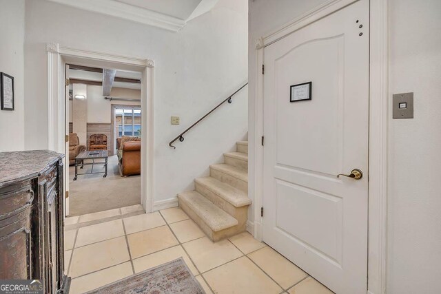 stairway with tile patterned floors, ornamental molding, and beamed ceiling