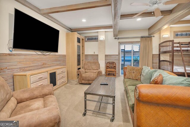 carpeted living room featuring beam ceiling, wood walls, and ceiling fan