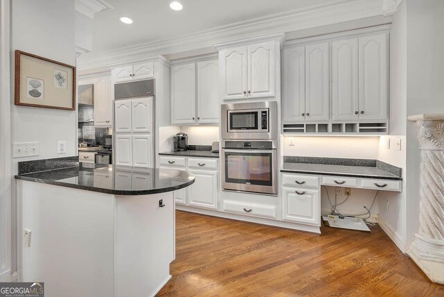 kitchen featuring kitchen peninsula, crown molding, built in appliances, white cabinetry, and light wood-type flooring