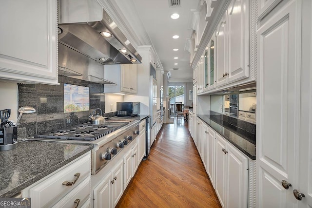 kitchen featuring white cabinetry, ventilation hood, dark stone countertops, wood-type flooring, and crown molding