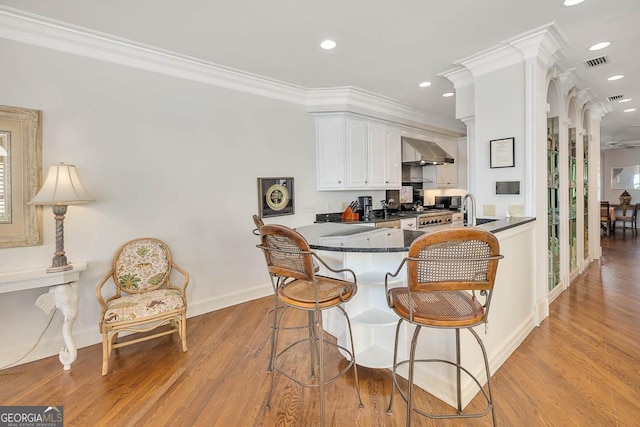kitchen with white cabinets, kitchen peninsula, wall chimney exhaust hood, and crown molding