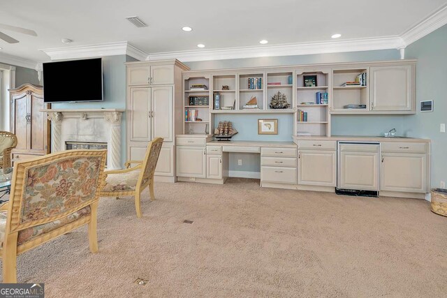 office area with ceiling fan, light colored carpet, ornamental molding, and built in desk