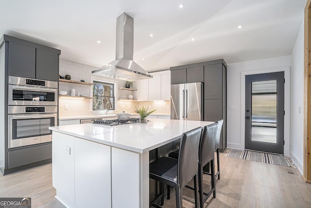 kitchen featuring island range hood, a center island, a kitchen breakfast bar, stainless steel appliances, and decorative backsplash