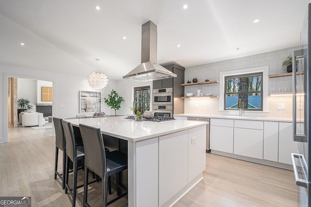 kitchen featuring white cabinetry, tasteful backsplash, island range hood, a kitchen island, and vaulted ceiling