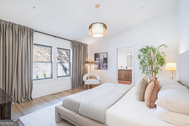 bedroom featuring vaulted ceiling, light wood-type flooring, and ensuite bath