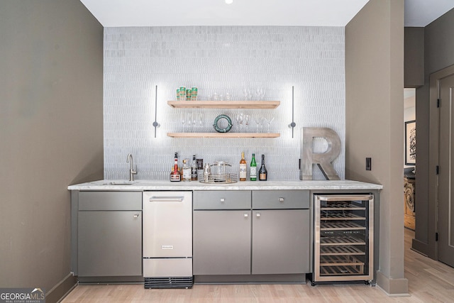 bar with light hardwood / wood-style flooring, gray cabinets, and beverage cooler