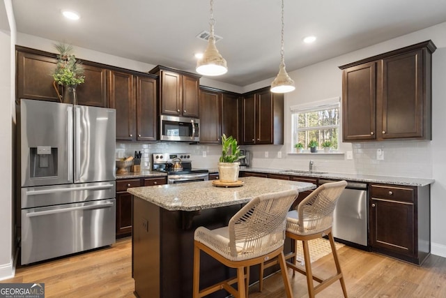 kitchen with pendant lighting, appliances with stainless steel finishes, a kitchen island, light hardwood / wood-style floors, and a kitchen breakfast bar