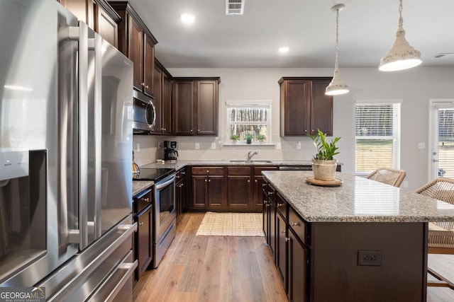 kitchen with stainless steel appliances, decorative light fixtures, light hardwood / wood-style flooring, a breakfast bar, and a center island