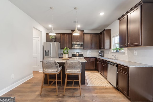 kitchen with appliances with stainless steel finishes, a kitchen island, sink, hanging light fixtures, and light stone counters