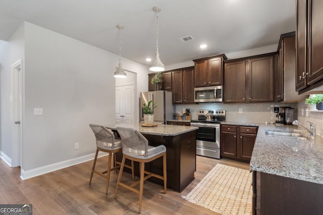 kitchen featuring decorative light fixtures, a center island, sink, light wood-type flooring, and stainless steel appliances