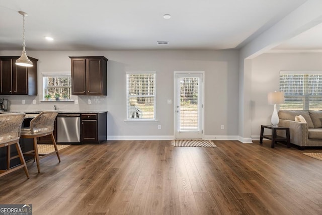 kitchen with backsplash, dark hardwood / wood-style floors, stainless steel dishwasher, dark brown cabinetry, and light stone counters