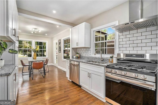 kitchen featuring wall chimney range hood, sink, light stone countertops, appliances with stainless steel finishes, and white cabinets