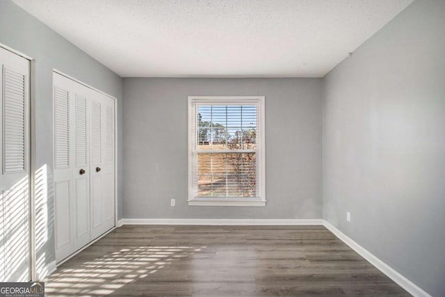113 Rue Fontaine Unit 113, Lithonia, GA 30038 - unfurnished bedroom with wood finished floors, a textured ceiling, baseboards, and two closets