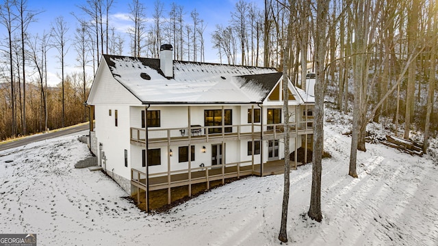 snow covered rear of property featuring a balcony and a wooden deck