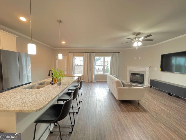 kitchen with pendant lighting, stainless steel fridge, crown molding, and an island with sink