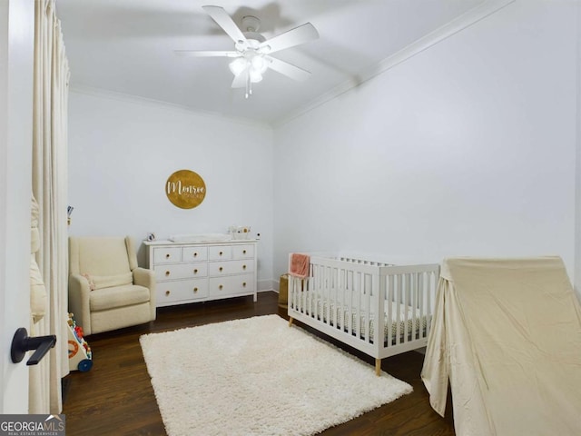 bedroom featuring ceiling fan, dark wood-type flooring, ornamental molding, and a crib