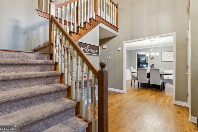 stairs with hardwood / wood-style flooring, ornamental molding, and a notable chandelier