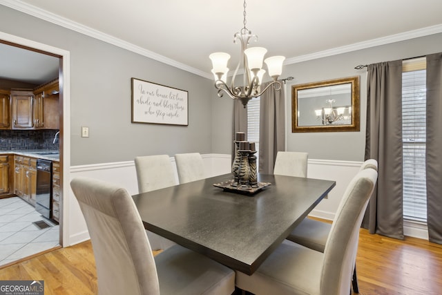 dining space featuring sink, crown molding, a chandelier, and light wood-type flooring