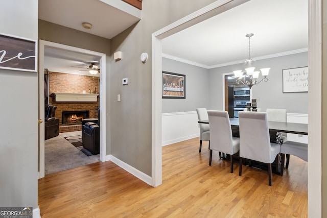 dining area with a brick fireplace, ornamental molding, ceiling fan with notable chandelier, and light hardwood / wood-style flooring