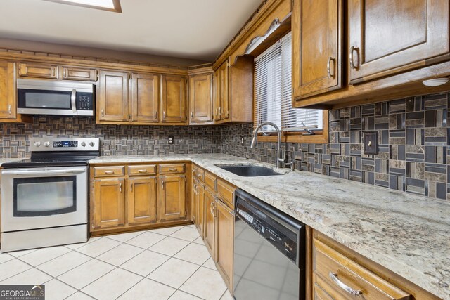 kitchen with light tile patterned floors, appliances with stainless steel finishes, backsplash, light stone countertops, and sink