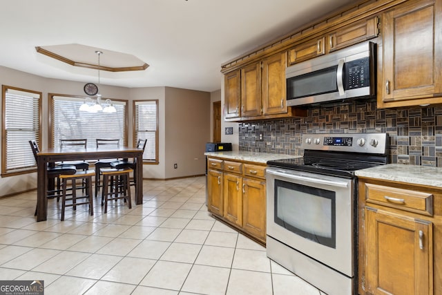 kitchen with tasteful backsplash, a notable chandelier, a tray ceiling, stainless steel appliances, and light tile patterned floors