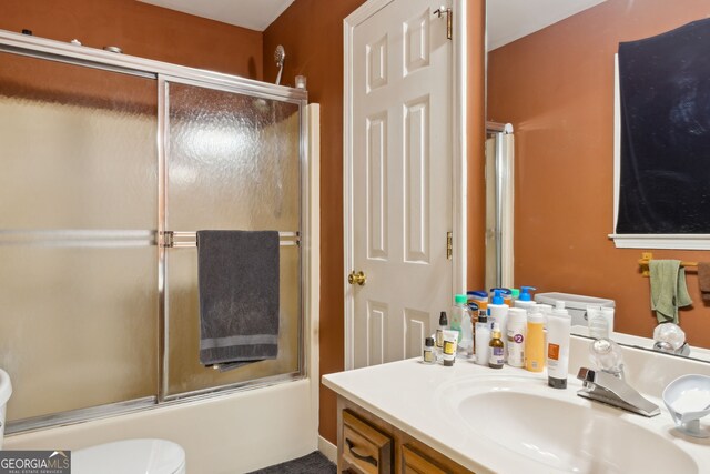 full bathroom featuring combined bath / shower with glass door, vanity, and toilet