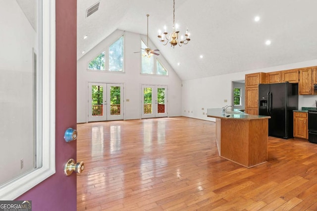 kitchen with light hardwood / wood-style floors, a center island with sink, black refrigerator with ice dispenser, high vaulted ceiling, and french doors