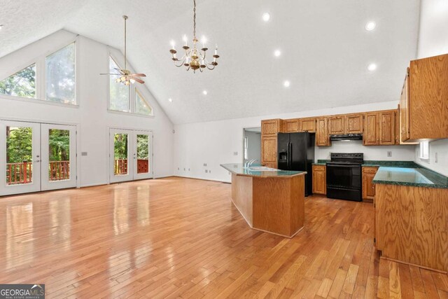 kitchen featuring an island with sink, french doors, high vaulted ceiling, ceiling fan with notable chandelier, and black appliances