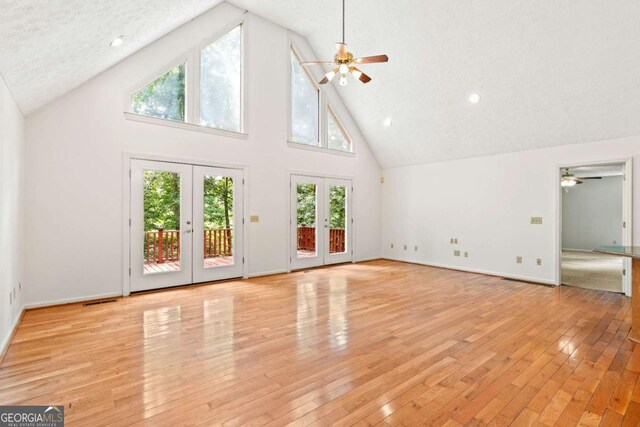 unfurnished living room featuring high vaulted ceiling, light hardwood / wood-style floors, a textured ceiling, and french doors