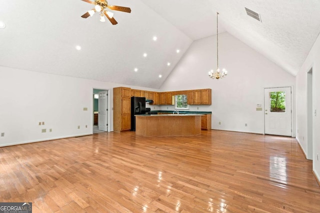 kitchen with a center island, black refrigerator with ice dispenser, hanging light fixtures, high vaulted ceiling, and light hardwood / wood-style flooring