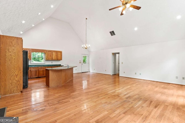 kitchen with a center island with sink, black refrigerator, high vaulted ceiling, pendant lighting, and light hardwood / wood-style flooring