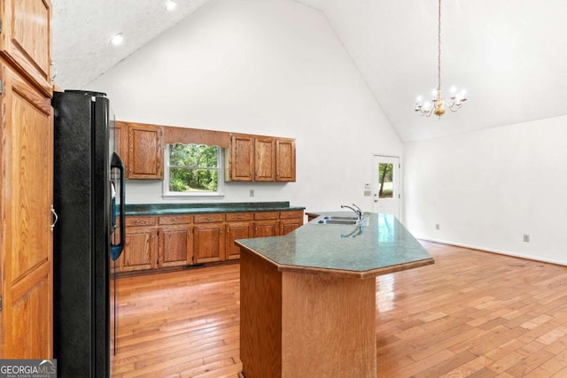 kitchen with high vaulted ceiling, sink, black fridge, and an island with sink