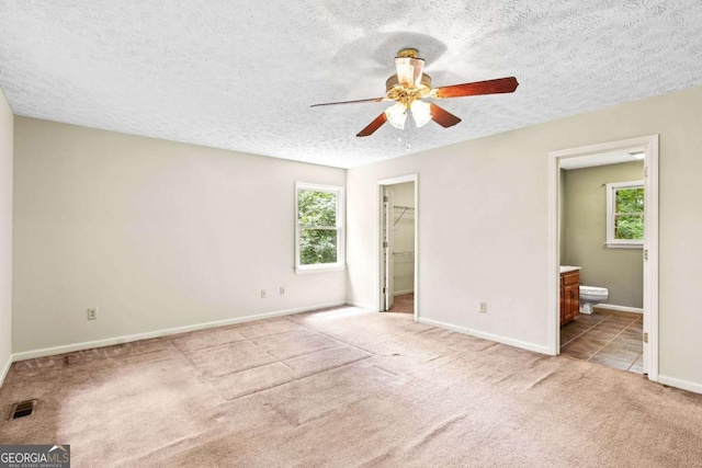 unfurnished bedroom with ceiling fan, multiple windows, light colored carpet, and ensuite bath