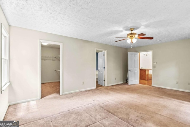 unfurnished bedroom with a spacious closet, a textured ceiling, light carpet, a closet, and ceiling fan