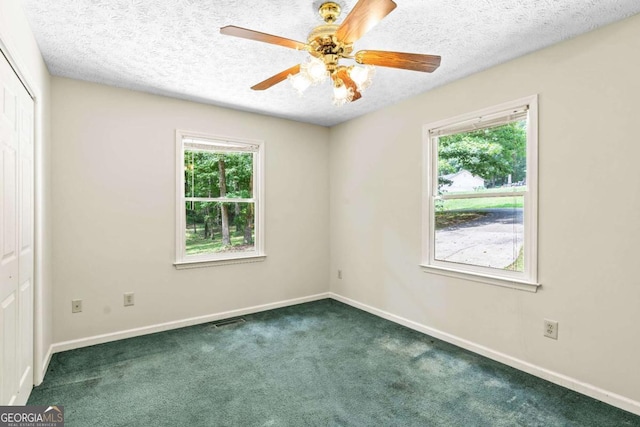 empty room with ceiling fan, dark carpet, and a textured ceiling