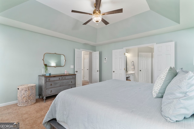 carpeted bedroom with ceiling fan, ensuite bath, and a tray ceiling