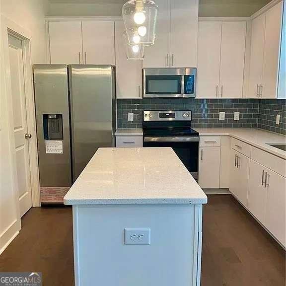 kitchen featuring decorative backsplash, hanging light fixtures, appliances with stainless steel finishes, white cabinets, and light stone counters