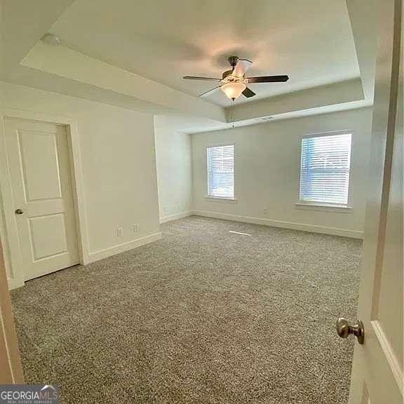 carpeted empty room with ceiling fan and a tray ceiling