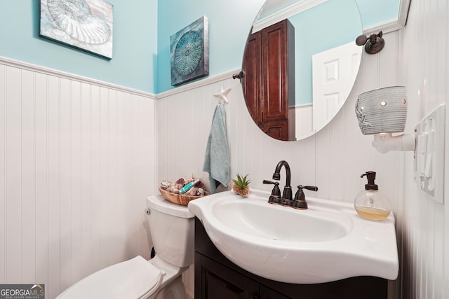 bathroom with toilet, vanity, and wood walls