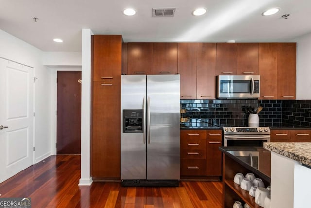 kitchen featuring backsplash, dark hardwood / wood-style floors, dark stone counters, and stainless steel appliances