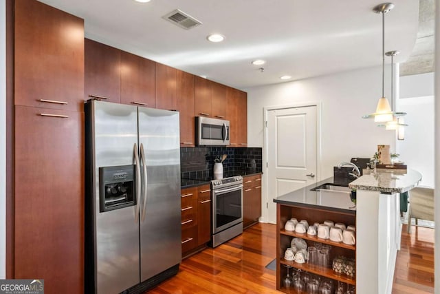 kitchen with dark wood-type flooring, stainless steel appliances, sink, backsplash, and kitchen peninsula