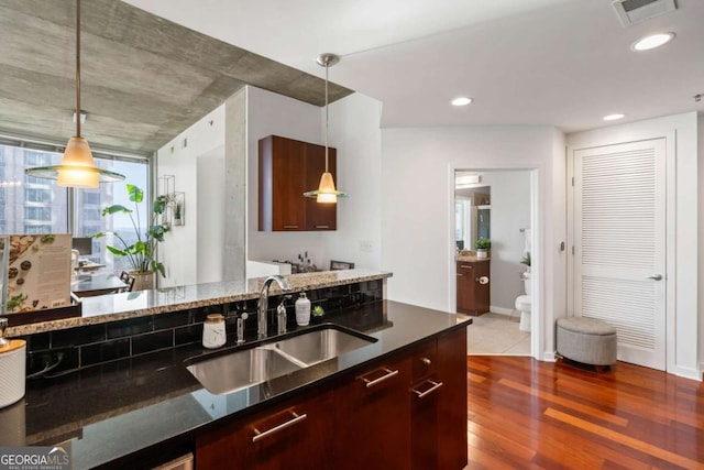 kitchen with dark wood-type flooring, sink, hanging light fixtures, and dark stone counters