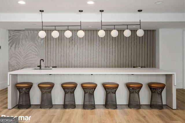 kitchen featuring sink, decorative light fixtures, a kitchen bar, and light hardwood / wood-style floors