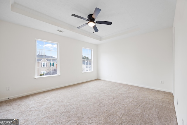 carpeted spare room with ceiling fan, crown molding, and a tray ceiling