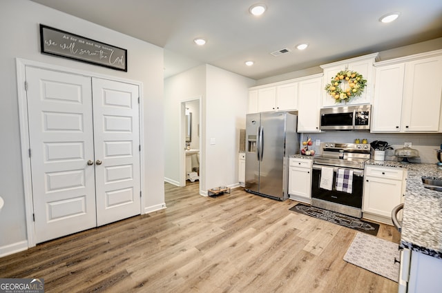 kitchen featuring white cabinetry, appliances with stainless steel finishes, decorative backsplash, light wood-type flooring, and light stone counters