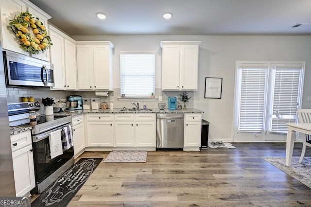 kitchen featuring light stone countertops, stainless steel appliances, white cabinets, and sink